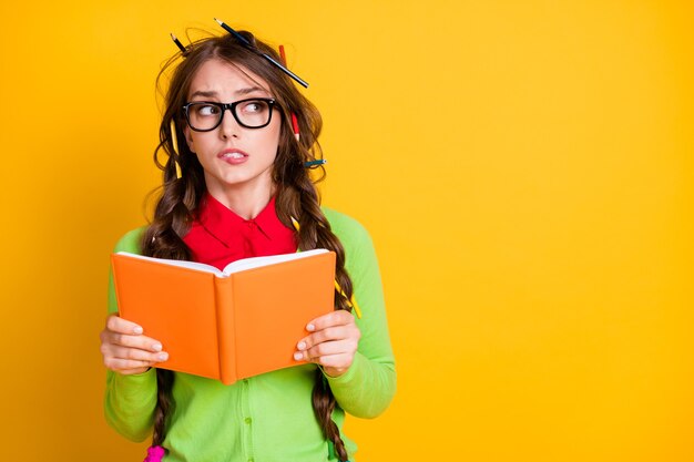 Portret van aantrekkelijke funky nerveuze tienermeisje lezen werkboek denken bijten lip kopie ruimte geïsoleerd over heldere gele kleur achtergrond
