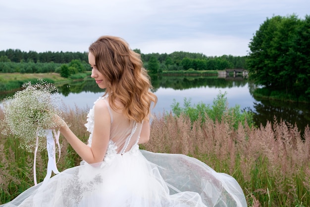 Foto portret van aantrekkelijke glimlachende jonge stijlvolle bruid in witte modieuze trouwjurk met bruiloft boeket