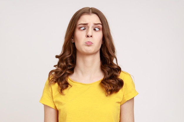 Portret van aantrekkelijke grappige domme jonge vrouw in geel T-shirt met schele ogen, heeft een stom stom gezicht, ongemakkelijke verwarde komische uitdrukking. Indoor studio opname geïsoleerd op een grijze achtergrond.