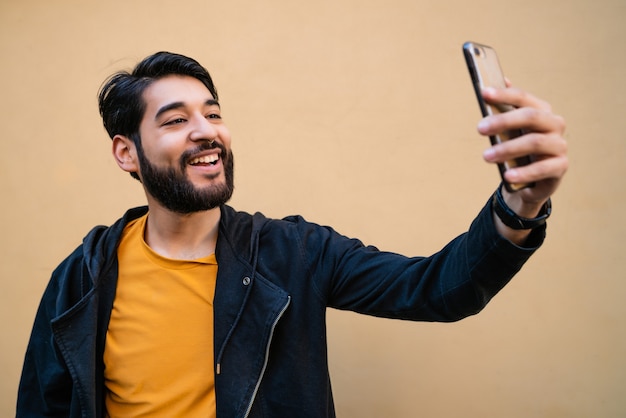 Portret van aantrekkelijke jonge man die selfies met zijn mophile telefoon neemt tegen gele muur. Technologie concept.