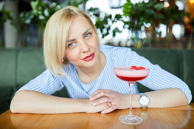 Portret van aantrekkelijke jonge vrouw die cocktail drinkt in café binnen Mooie blonde vrouw die aan de bar ontspant en een cocktail drinkt