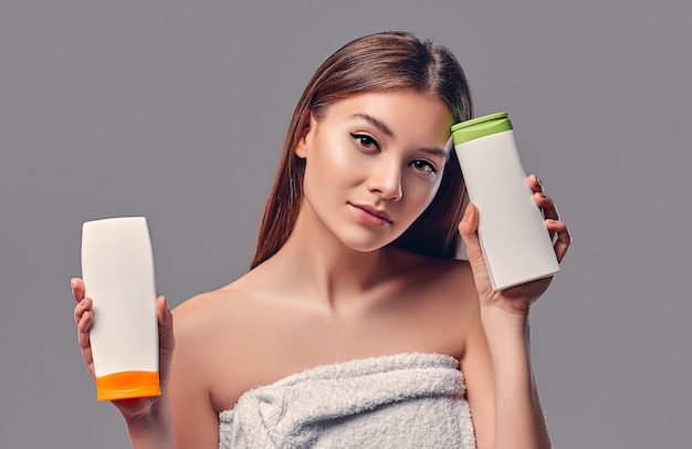 Portret van aantrekkelijke jonge vrouw met twee shampoos op grijze achtergrond. Keuze maken. vrouwen zorg