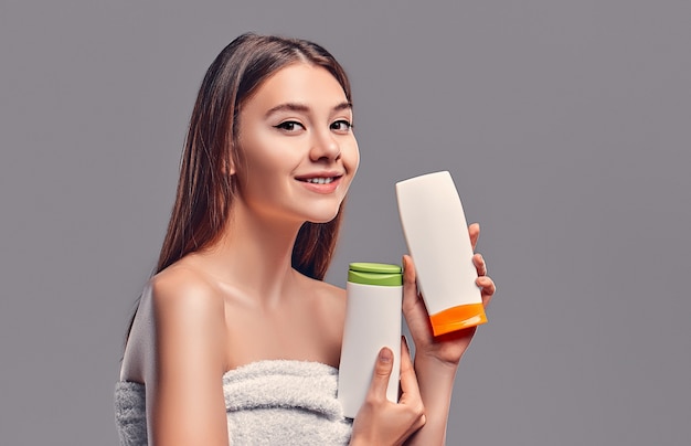 Portret van aantrekkelijke jonge vrouw met twee shampoos op grijze achtergrond. Keuze maken. vrouwen zorg