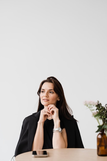 Portret van aantrekkelijke jonge vrouw op witte achtergrond dromerig vrolijk meisje gekleed in zakelijke stijl zit aan tafel in wit café