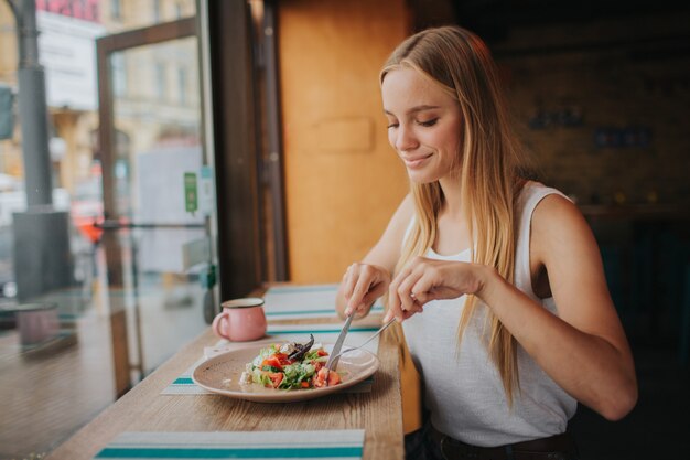 Portret van aantrekkelijke Kaukasische glimlachende vrouw die salade eet