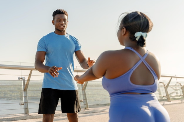 Portret van aantrekkelijke knappe Nigeriaanse trainer die plus size vrouw traint in sportkleding buitenshuis