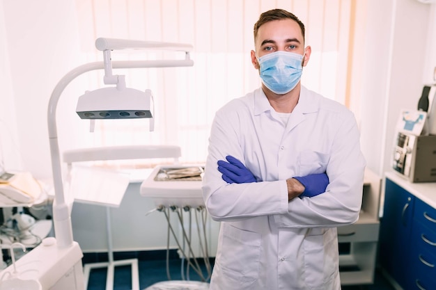 Portret van aantrekkelijke knappe tandarts met kapsel in beschermend masker witte laboratoriumjas