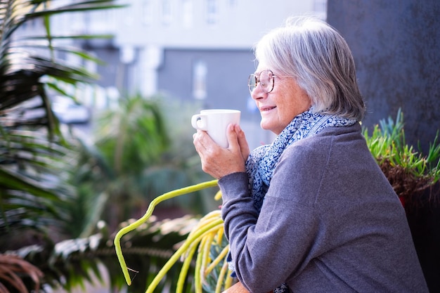 Portret van aantrekkelijke, ontspannen senior vrouw met bril die buiten warme koffie of thee drinkt