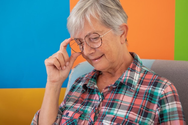 Portret van aantrekkelijke senior witharige vrouw in geruit hemd om thuis te kijken naar beneden peinzende hipster glimlachende grootmoeder ontspannen op fauteuil