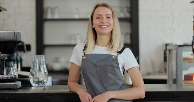 Portret van aantrekkelijke vrouw bariata staande in het openen van de coffeeshop en glimlachend camera kijken. Koffiehuis interieur op de achtergrond.