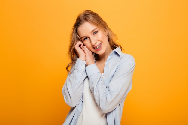 Portret van aantrekkelijke vrouw die steunen dragen die op camera met spontane verleidelijke blik stellen, dat over gele achtergrond wordt geïsoleerd