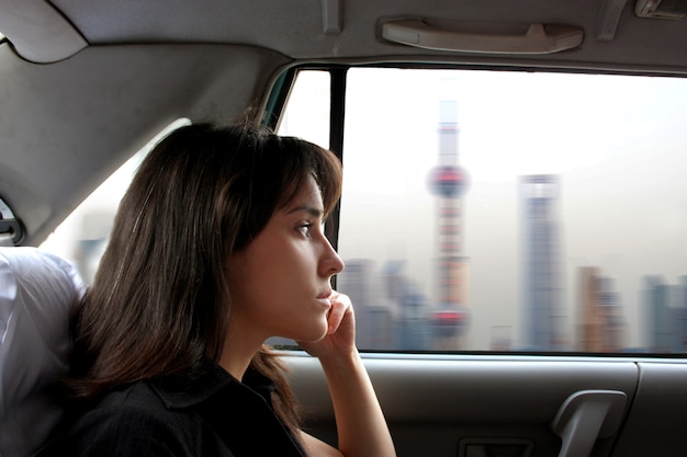 Portret van aantrekkelijke vrouw gezet in een taxi en bekijkend chinese stad