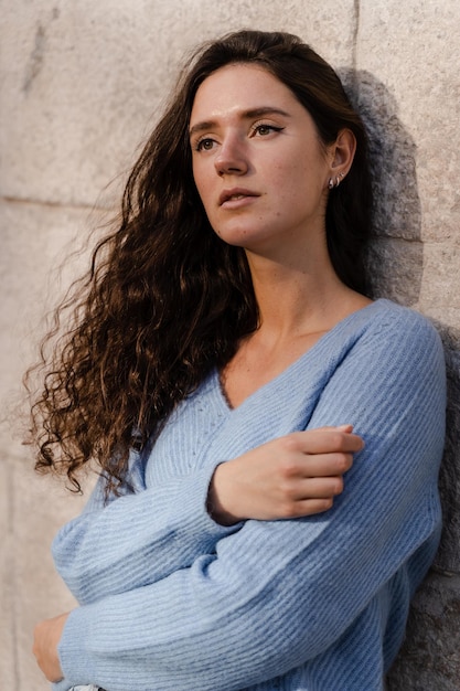 Portret van aantrekkelijke zakenvrouw met krullend haar poseert op grijze muur achtergrond Zelfverzekerd meisje model weared in blauwe trui poseert buiten in de stad