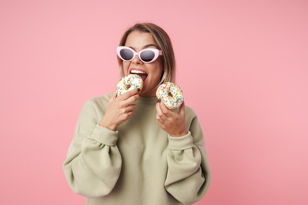Portret van aardige gelukkige vrouw in zonnebril die donuts eet