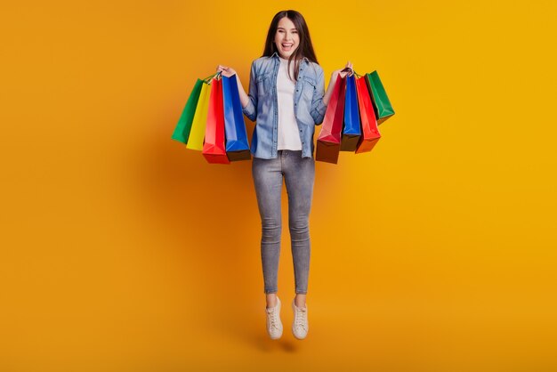 Portret van actieve positieve meisje springen houden winkelen koopjes geïsoleerd op gele achtergrond