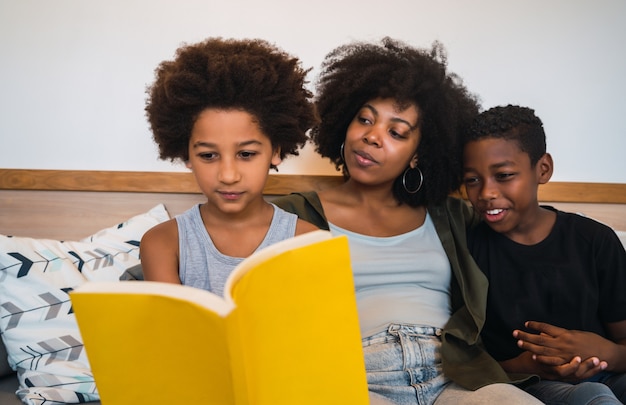 Portret van Afro-Amerikaanse moeder die een boek leest aan haar kinderen thuis