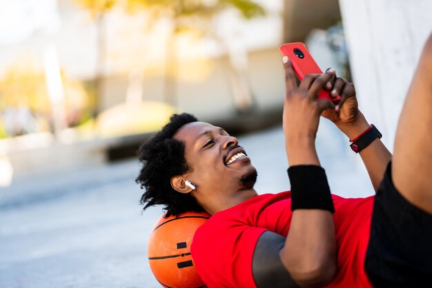 Portret van afro atleet man met behulp van zijn mobiele telefoon tijdens het leggen op de vloer na een training buitenshuis. Sport en een gezonde levensstijl.