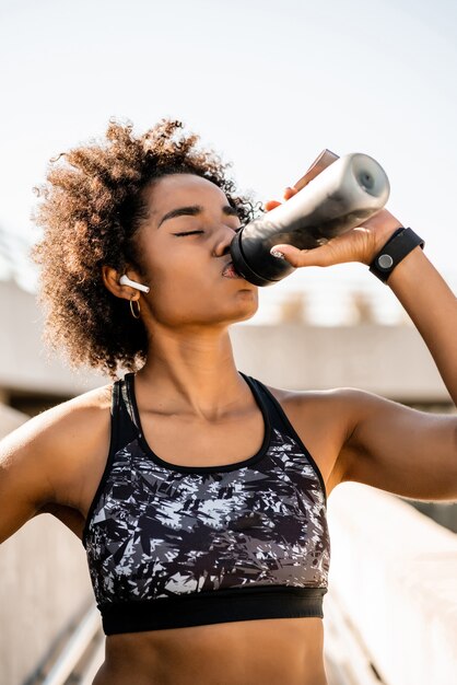 Portret van afro atleet vrouw drinkwater na training buitenshuis. Sport en een gezonde levensstijl.