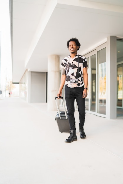 Portret van afro toeristische man met koffer tijdens het buiten lopen op straat. Toerisme concept.