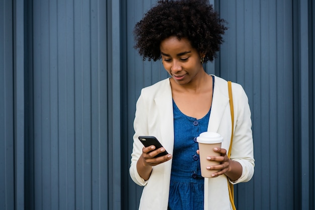 Portret van afro zakenvrouw met behulp van haar mobiele telefoon terwijl ze buiten op straat staat.