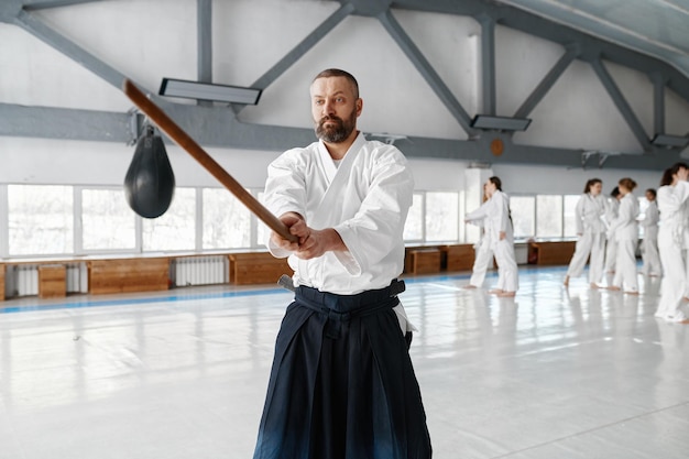 Portret van aikido sensei meester met houten zwaard bij groepstraining. Leren vechten met bamboeboken