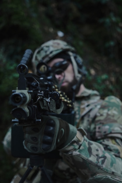 Portret van airsoft-speler in professionele uitrusting in helm gericht op slachtoffer met pistool in het bos. Soldaat met wapens in oorlog