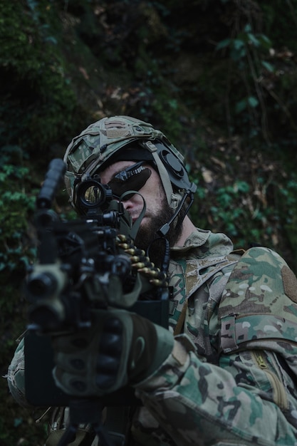 Portret van airsoft-speler in professionele uitrusting in helm gericht op slachtoffer met pistool in het bos. Soldaat met wapens in oorlog