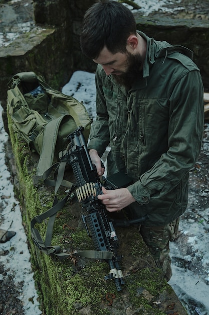 Portret van airsoft-speler in professionele uitrusting laadt een pistool met kogels in het bos. Soldaat met wapens in oorlog