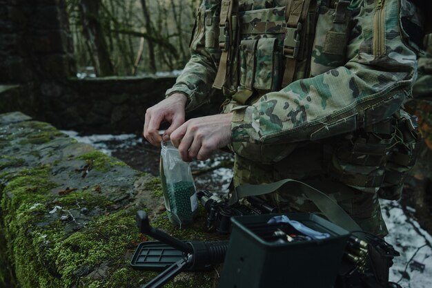 Portret van airsoft-speler in professionele uitrusting laadt een pistool met kogels in het bos. Soldaat met wapens in oorlog