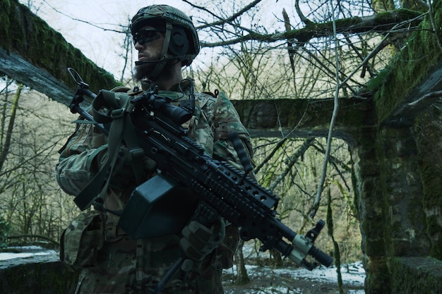 Portret van airsoft-speler in professionele uitrusting met machinegeweer in het bos. Soldaat met wapens in oorlog