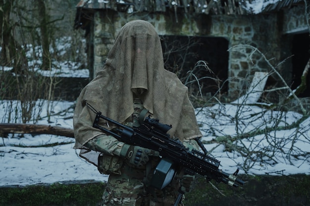 Portret van airsoft-speler in professionele uitrusting met machinegeweer in het bos.