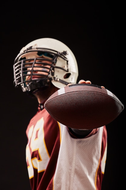 Portret van American football-speler met bal tegen zwarte achtergrond