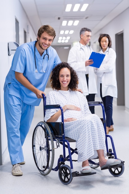 Portret van arts die een zwangere vrouw op rolstoel duwt