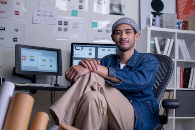 Portret van Aziatische man grafisch ontwerper zittend en glimlachend terwijl hij naar de camera kijkt