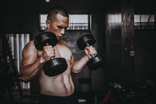 Portret van aziatische man grote spier in de sportschoolthailand mensentraining voor een goede gezondheidbody weight trainingfitness in de sportschool conceptprank naar buikspierenhef dumpbell op