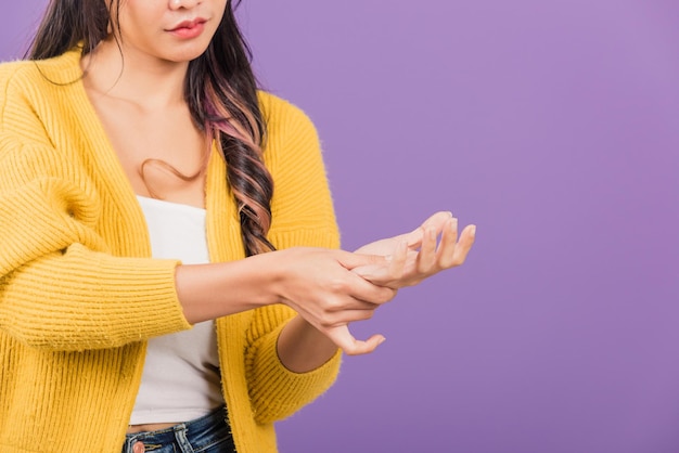 Portret van Aziatische mooie jonge vrouw die lijdt aan pijn in handpalm of handen en haar pijnlijke handen masseert, studio opname geïsoleerd op paarse achtergrond, gezondheidszorg artritis concept