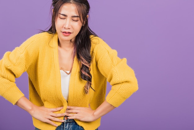 Portret van Aziatische mooie jonge vrouw heeft buikpijn, vrouwelijke buikpijn die lijdt aan buikpijn, studio opname geïsoleerd op paarse achtergrond, Gezondheid en medisch gastritis concept