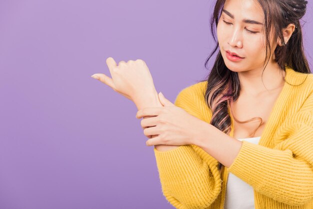 Portret van Aziatische mooie jonge vrouw verdrietig met polspijn van carpaaltunnelsyndroom, vrouwelijke handblessure die pijn voelt, studio-opname geïsoleerd op paarse achtergrond, gezondheidszorg en medisch concept