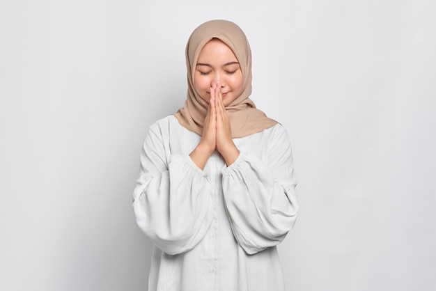 Portret van Aziatische moslimvrouw hand in hand bidden in de buurt van mond geïsoleerd op witte achtergrond