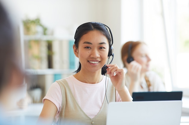 Portret van Aziatische operator in hoofdtelefoon glimlachen tijdens het werken in callcenter