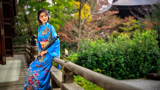 Portret van Aziatische vrouw die Japanse blauwe kimono en paraplu op holdingshand draagt