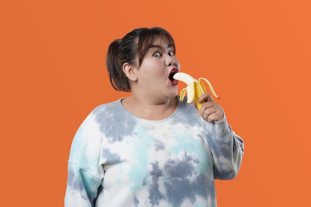 Portret van Aziatische vrouw met banaan, geïsoleerd op een oranje achtergrond, concept van gezonde voeding