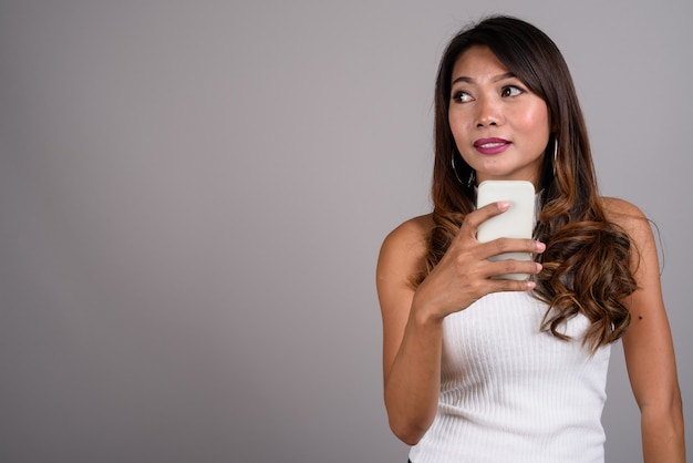 Portret van Aziatische vrouw met golvend haar die telefoon met behulp van