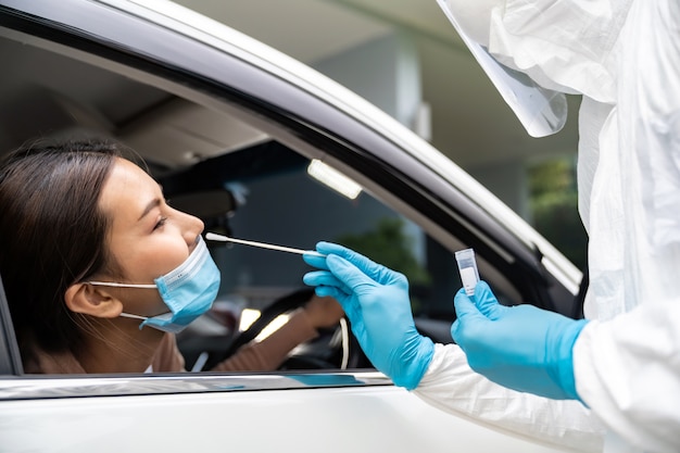 Portret van Aziatische vrouw rijdt door coronavirus covid-19-test door medisch personeel met PPE-pak door neuszwabber. Nieuwe normale gezondheidszorg door service en medisch concept.