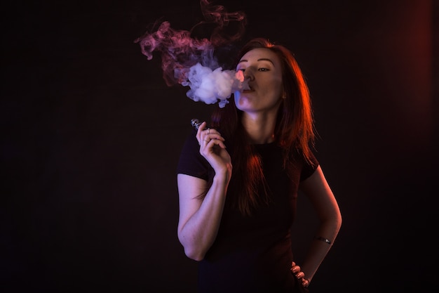 Portret van aziatische vrouw roken vape of e-sigaret in neonlicht op zwarte achtergrond.