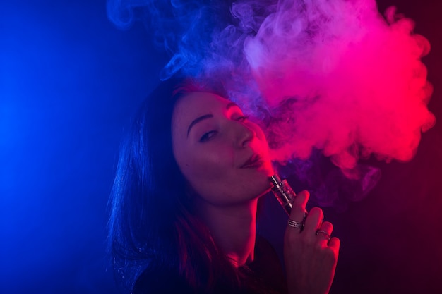 Portret van Aziatische vrouw roken vape of e-sigaret in neonlicht op zwarte achtergrond.