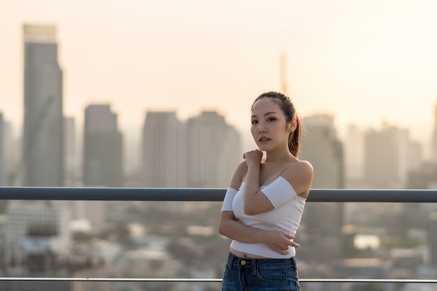 Portret van Aziatische Yong-vrouw in sexy manierkostuum die zich op het dak over citysca bevinden