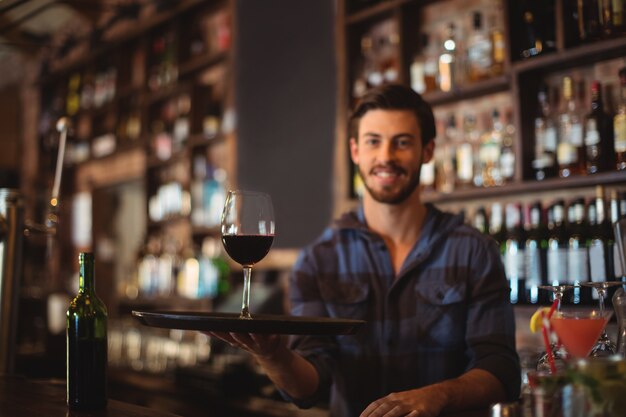 Portret van barman met een dienblad met een glas rode wijn