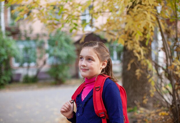 Portret van basisschoolstudent met rode aktentas op de herfstdag