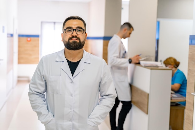 Portret van bebaarde arts in witte scrubs Medisch werker staat in ziekenhuisgang